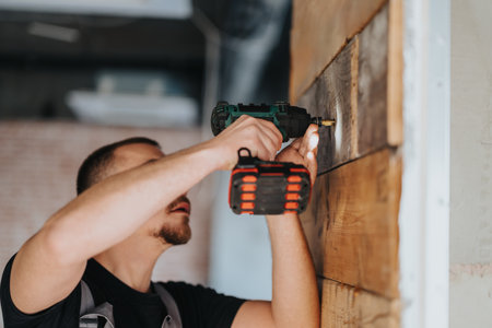 Manual laborer using a cordless drill to secure wooden panels inside a building.の写真素材