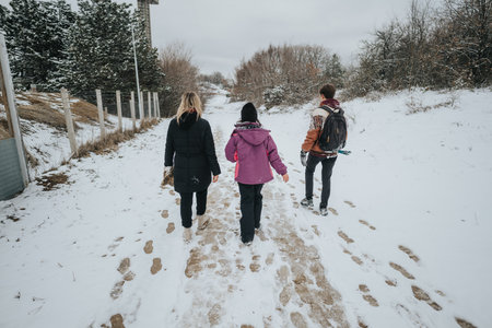Three friends walking together on a snowy forest path, dressed warmly in winter clothing, enjoying the serene natural surroundings on a cold and overcast day.の写真素材