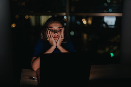Tired woman working late at night on her laptop in a dim roomの写真素材