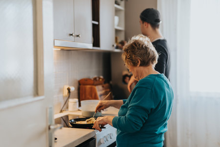 Elderly woman cooking in the kitchen while a young man stands nearby.の写真素材
