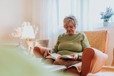 Senior woman reading a book while relaxing in a cozy living room settingの写真素材