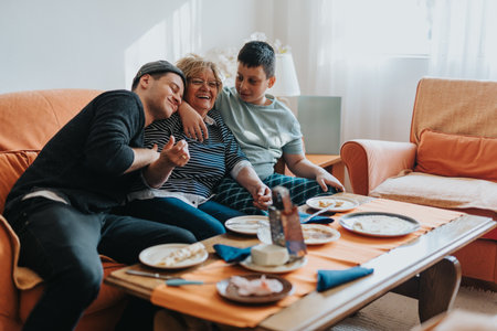 Senior woman sitting with loved ones on a cozy couch sharing a meal and joyful moments togetherの写真素材