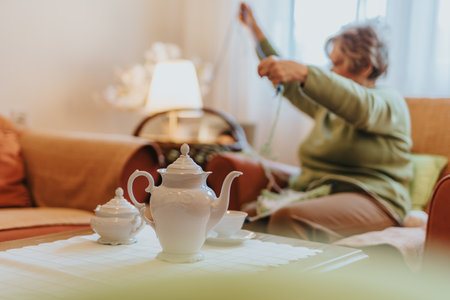 Senior woman knitting in cozy living room with porcelain tea setの写真素材