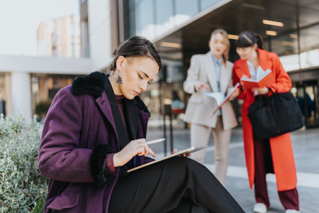 Three professional businesswomen discussing work outdoors with a focus on teamworkの写真素材