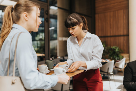 Two businesswomen discussing over coffee in a modern cafe setting during daytime.の写真素材