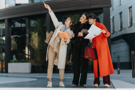 Three female professionals discuss plans outdoors with documentsの写真素材