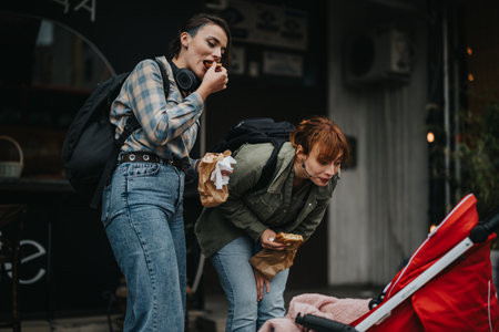 Women enjoying street food while looking at baby in strollerの写真素材