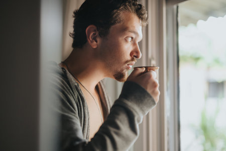 Young man relaxing at home while enjoying coffee by the window in natural lightの写真素材