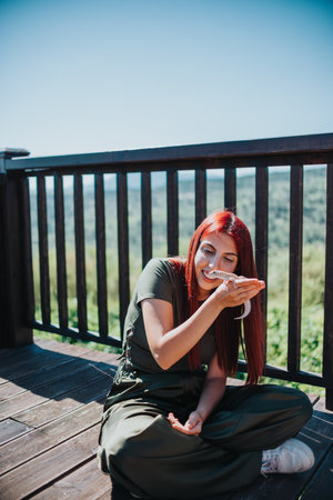 Young woman enjoying a playful moment with a lizard on a wooden deck overlooking natureの写真素材