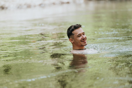 Young man enjoying a refreshing swim in a natural river settingの写真素材