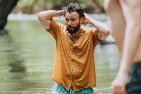 Man standing in river wearing orange shirt with natural outdoor surroundings