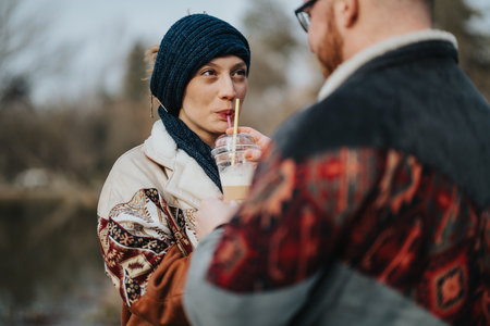 Couple enjoying a shared drink outdoors in winter attireの写真素材