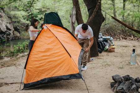Friends collaborating to set up an orange tent at a camping siteの写真素材