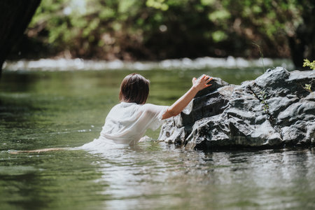 Woman in white shirt resting on rock surrounded by relaxing river sceneryの写真素材