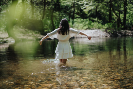 Woman in white dress enjoying nature in a serene forest riverの写真素材