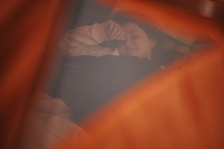 Woman resting peacefully in an orange tent during a serene outdoor adventureの写真素材