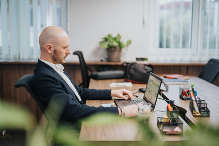 Businessman working on a laptop at a modern office desk with organized suppliesの写真素材