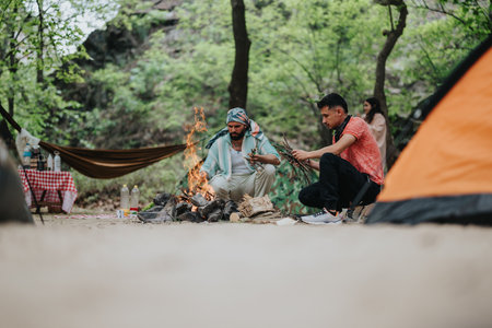 Group of friends enjoying campfire activities in a forest camping settingの写真素材