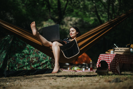 Woman relaxing in a hammock while working on her laptop in the forest