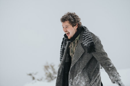 Joyful man standing outdoors in snowy weather wearing a grey coat and scarfの写真素材