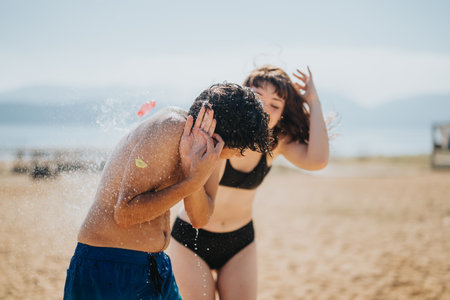 Friends laughing and splashing water on a sunny sandy beach dayの写真素材