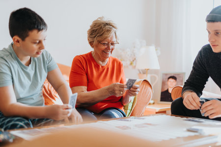 A joyful elderly woman engaging in a card game with two young boys in a cozy living room settingの写真素材
