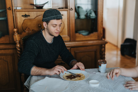 Man preparing a chocolate spread on a pancake in a cozy home environmentの写真素材