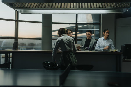 A group of business people in a modern office environment engage in a collaborative discussion while standing around a table under stylish lighting.の写真素材