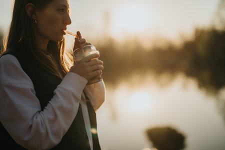 Young woman enjoying a drink by a lake during golden hour
