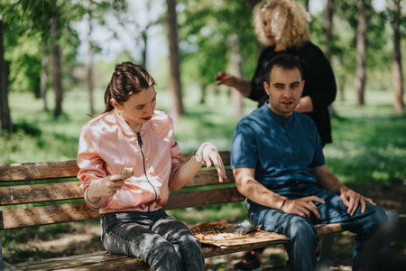 Group of friends enjoying a casual meal on a park bench surrounded by greeneryの写真素材