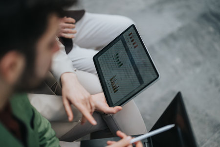Two people discussing charts and graphs displayed on a tablet in an office settingの写真素材