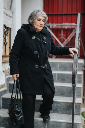 Elderly woman dressed warmly descending stairs outdoors with bagの写真素材