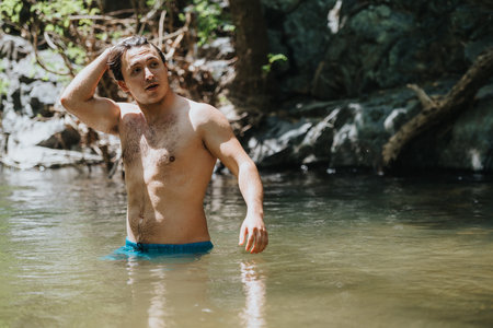 Young man enjoying a refreshing swim in a natural forest streamの写真素材