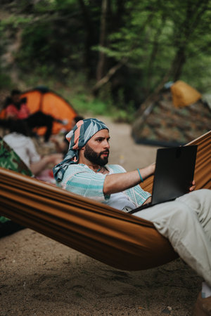 Man relaxing in a hammock while using a laptop at a campsiteの写真素材