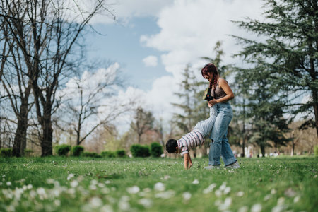 Mother assisting son with exercises in park under clear skyの写真素材