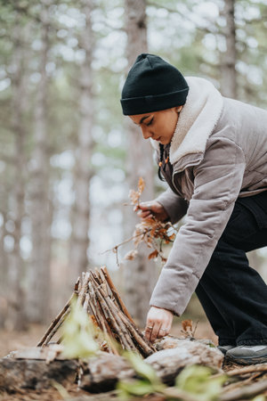 Woman building a small campfire structure in a serene forest settingの写真素材