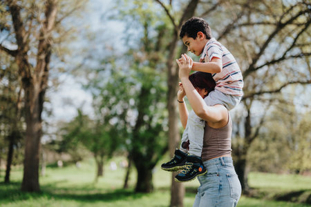 Mother carrying her child on shoulders in a green parkの写真素材