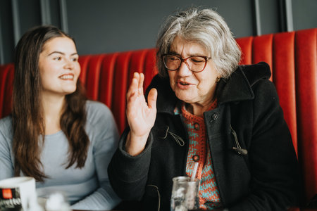 Elderly woman sharing stories with a young companion in a cozy cafeの写真素材