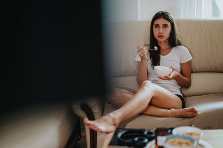 Young woman relaxing on a sofa while eating yogurt at homeの写真素材
