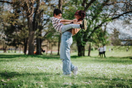 Mother joyfully lifts her child in a sunny green parkの写真素材