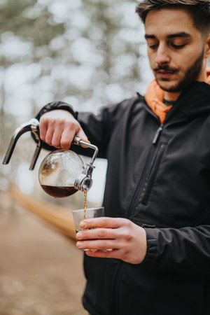 Young Man Pouring Coffee from a Glass Pot While Enjoying a Winter Picnic