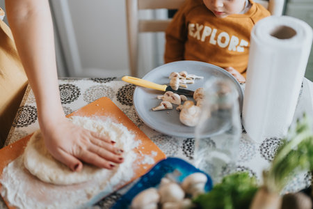 Parent and child preparing pizza dough in the kitchen with mushrooms and ingredients.の写真素材
