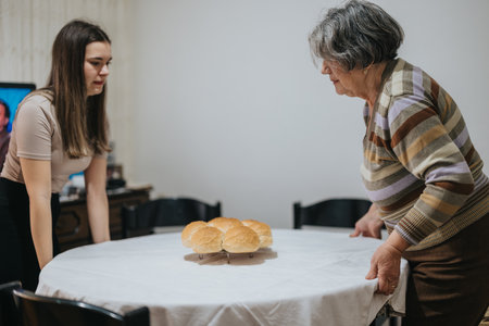 Senior woman and younger female preparing a table with bread in a cozy dining settingの写真素材