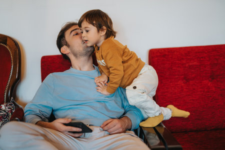 Father and young child enjoying tender family moment on a cozy living room red sofaの写真素材