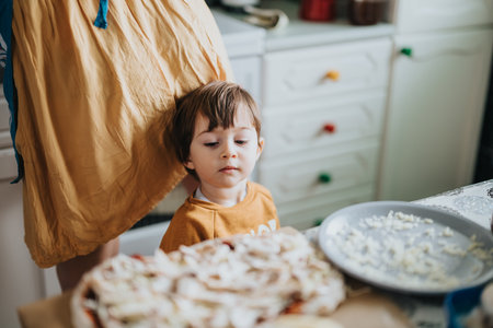 Young child standing near a table preparing food in a cozy home kitchen settingの写真素材