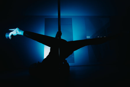 Silhouette of a dancer performing pole art under deep blue lightingの写真素材