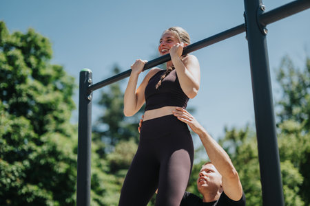 Woman practicing pull-ups outdoors assisted by instructor on a sunny dayの写真素材