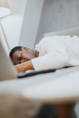 Man in a cozy sweater resting on a desk with a laptop in a minimalistic interiorの写真素材