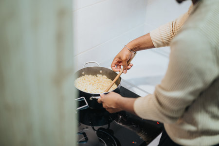 Person Cooking Pasta on a Stove in a Modern Home Kitchenの写真素材