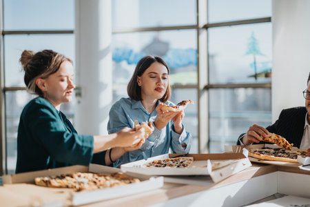 Team enjoying pizza together during a casual office lunchの写真素材